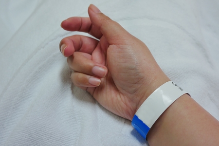A hand of adult Asian female patient with Hospital Bracelet while hospitalized and recovery from the surgery at the hospital. Close up.の写真素材