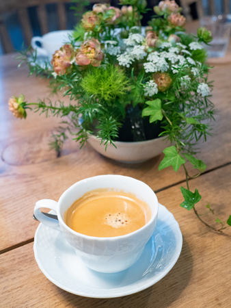 Freshly brew Cafe Latte or Cafe Au Lait coffee in a white porcelain ceramic cup with saucer on a rustic wooden table with flower background. Good for caffeine boost in the morning. Selective focus.の写真素材