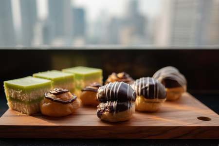 Assortment of desserts on wooden tray. Tasty and delicious layer cake and Cream Puff or profiterole with chocolate decoration against cityscape urban skyline background at rooftop bar.Selective focusの写真素材