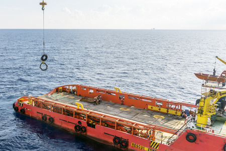 Anchor handling tug receiving anchor pennant wire from construction barge using barge crane