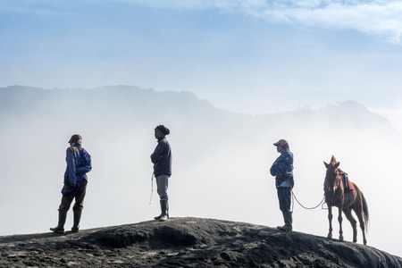 three horsemen resting on the sand dune with foggy / misty morning background at Bromo-Tengger-Semeru National Park, Indonesiaのeditorial素材