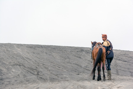 A tenggerese horseman walking his horse on dune with misty morning background after providing a...