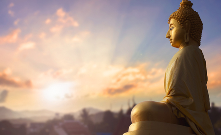 Buddha statue against sunrise and mountainous backgroundの写真素材