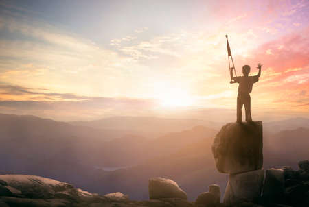 a disabled man standing up and raising his crutches over mountain sunset background