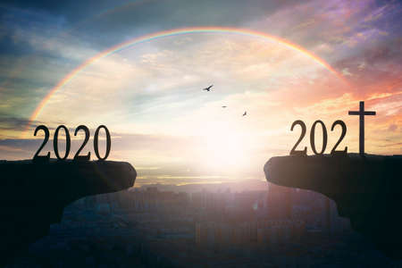 2021 concept: Silhouette of year 2021 and cross on mountain with city sunset background