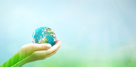 Human hands holding earth globe over blurred green nature and blue sky background.の写真素材