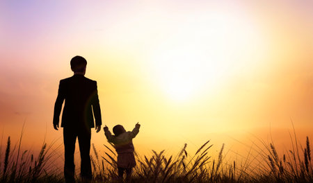 Silhouette of father and son standing on grass against sunset sky backgroundの写真素材
