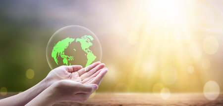 Earth day concept, A green earth globe in human hands over blurred beautiful nature backgroundの写真素材