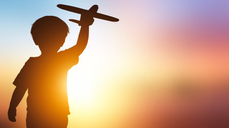 Silhouette of a boy playing with toy airplane on sunset backgroundの写真素材