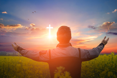 Christian man worshiping the christian cross in the field at sunsetの写真素材