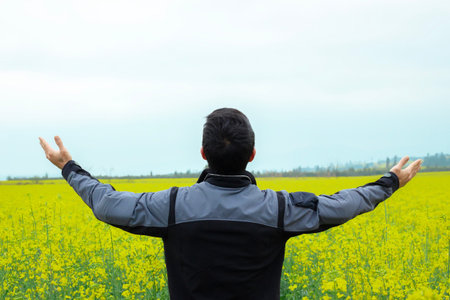 Young man with arms outstretched in a yellow field of flowers.