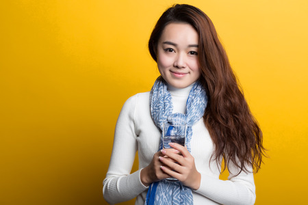 Yellow background, the Chinese girl holding a glass of water to drink, lively and lovely expressionの写真素材