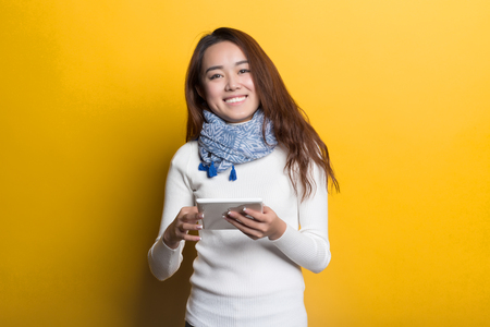 Young Chinese girl using cell phone on a yellow backgroundの写真素材