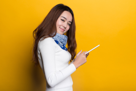 Young Chinese girl using cell phone on a yellow backgroundの写真素材