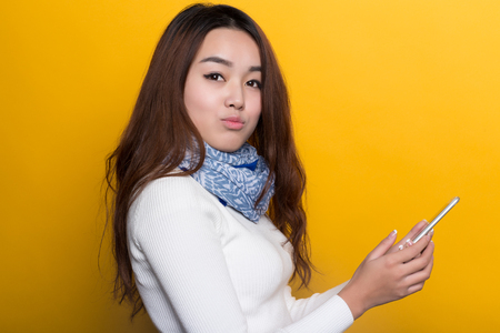 Use Young Chinese girl with a cell phone on a yellow background, expression of various expressionsの写真素材