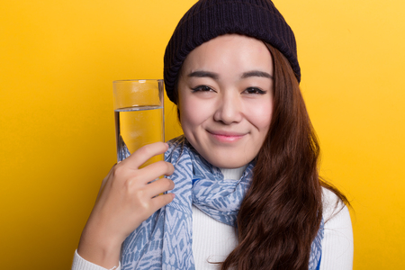 Yellow background, the Chinese girl holding a glass of water to drink, lively and lovely expressionの写真素材
