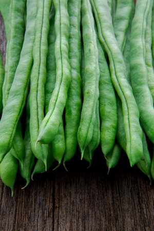 Fresh green vegetables beans with carrots on log tabletop