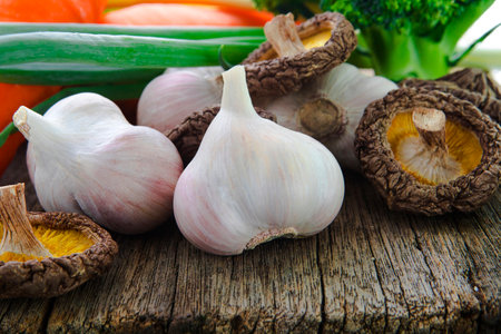 Shiitake mushrooms and garlic with diverse vegetables on log tableの写真素材