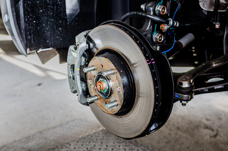 Front disc brake on car in process of new tire replacement. The rim is removed showing the front rotor and caliper