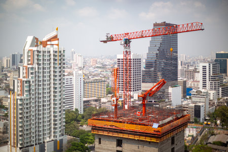 High-rise building construction with cranes against the urban skyline of a bustling Asian cityの写真素材