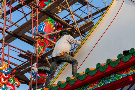 A rear view of a painter climbing up to paint the roof of a Chinese temple under repair.の写真素材