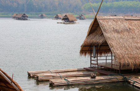 Tropical resort landscape featuring a wooden hut on the beach and a bungalow on the river with a boat near the sunset lagoonの写真素材