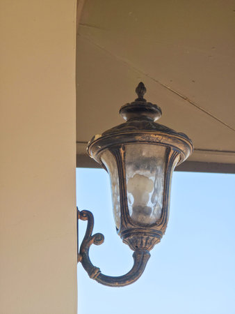 An antique-style bronze outdoor wall lantern mounted on a building corner against a clear blue sky.