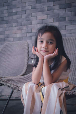 little girl sit chair looking at camera and touching cheeksの写真素材