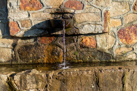 Water flowing from a fountain in a stone wall. Selective focus.