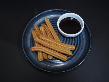 mexican churros with sauce served in a dish isolated on dark background top viewの写真素材