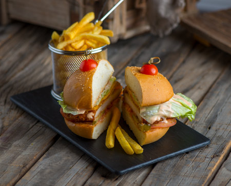 chicken burger with fries isolated on cutting board side view of fastfood on wooden backgroundの写真素材