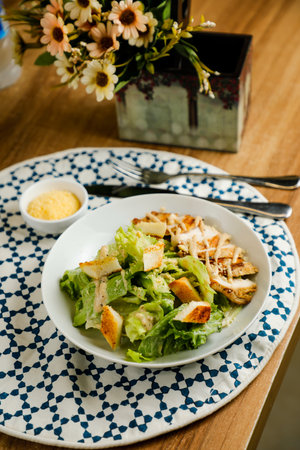 Caesar Salad or ceaser include chicken and spinach served in plate with flowers, knife and fork isolated on napkin side view of healthy green food on tableの写真素材