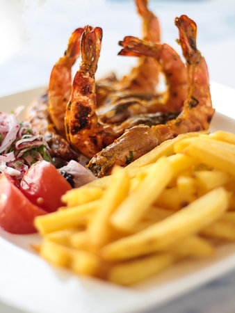 GRILLED PRAWNS with french fries, tomato and onion served in dish isolated on table closeup top view of grilled seafoodの写真素材