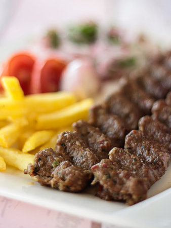 Lamb meat kabab or kebab with lemon, onion and french fries served in dish isolated wooden table top...