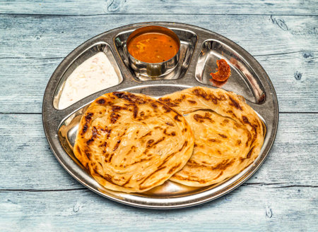 roti prata, paratha, parata, poratha with curry, raita and pickle served in thali dish isolated on wooden table top view of indian spicy foodの写真素材