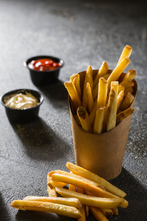 French Fries Bucket with dip sauce isolated on dark grey background side view of fast food