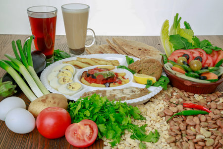 Egyptian Dynamite breakfast platter with flafel, marinated fried eggplant, boiled egg, hummus, potato, foul, beans, pita bread, salad and coffee drink isolated on table side viewの写真素材