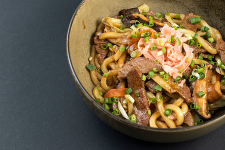 Beef Yakisoba Noodles topped with green onions served in bowl isolated dark background closeup side viewの写真素材