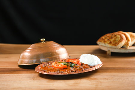 Turkish Meat Iskender Kebab topped with yogurt, tomato and green chilli served in golden sizzling plate with pita bread isolated on wooden table side view of traditional turkish foodの写真素材