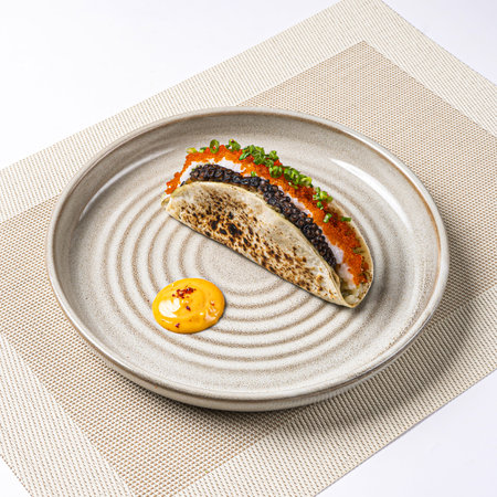 Caviar Taco topped with black caviar, herbs with a side of sauce served in plate on napkin side view on white backgroundの写真素材