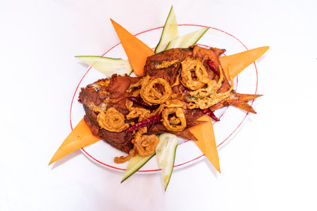 Fried Pomfret Fish garnished with crispy onion rings and red chili peppers served on white plate isolated on white background top view of thai and bangladeshi foodの写真素材