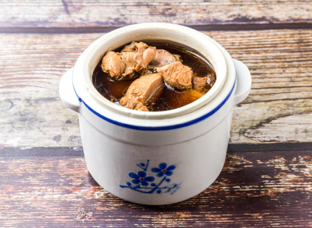 Snail head stewed in chicken soup served in clay pot broth isolated on wooden table side view of hong kong foodの写真素材