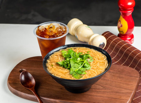 Clear noodles soup with coriander drink, and spoon served in pot isolated on wooden board side view...