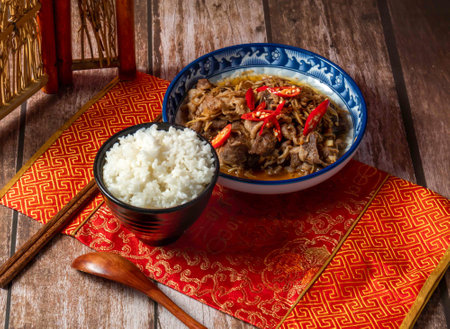 Stir fried beef with shredded ginger, white rice, red pepper, chopsticks and spoon served in dish side view on wooden tableの写真素材