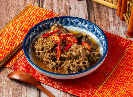 Stir fried beef with shredded ginger with red pepper, chopsticks and spoon served in dish isolated on napkin side view on wooden tableの写真素材