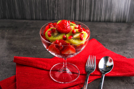 Colorful Fruit Salad with Strawberries, Kiwi, and Pomegranate Seeds served in bowl isolated on red napkin side view of healthy eating food on dark backgroundの写真素材