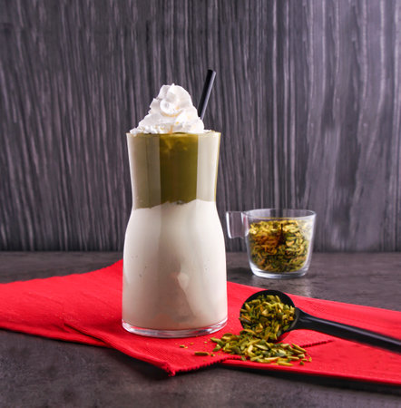 Pistachio Milkshake topped with whipped cream and chopped pistachios served in glass with straw on a red napkin side view of dessert drinkの写真素材