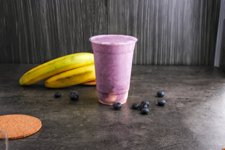 Refreshing Blueberry Banana Smoothie served in a clear plastic cup on a dark gray background side view of dessert drinkの写真素材