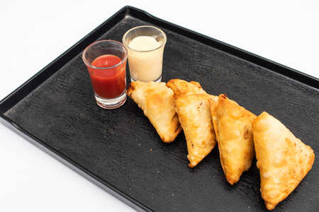 Chicken samosas with ketchup and raita chutney served on black tray isolated on white background...