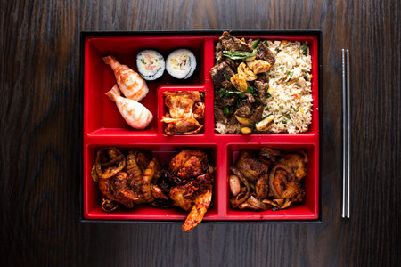 Bento Set include fried rice, Beef Bulgogi, grilled seafood and maki roll with chopsticks served in dish isolated on wooden table top view of korean foodの写真素材